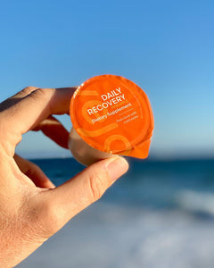 A hand holding the daily recovery blend in front of the pacific ocean in the morning sun. 