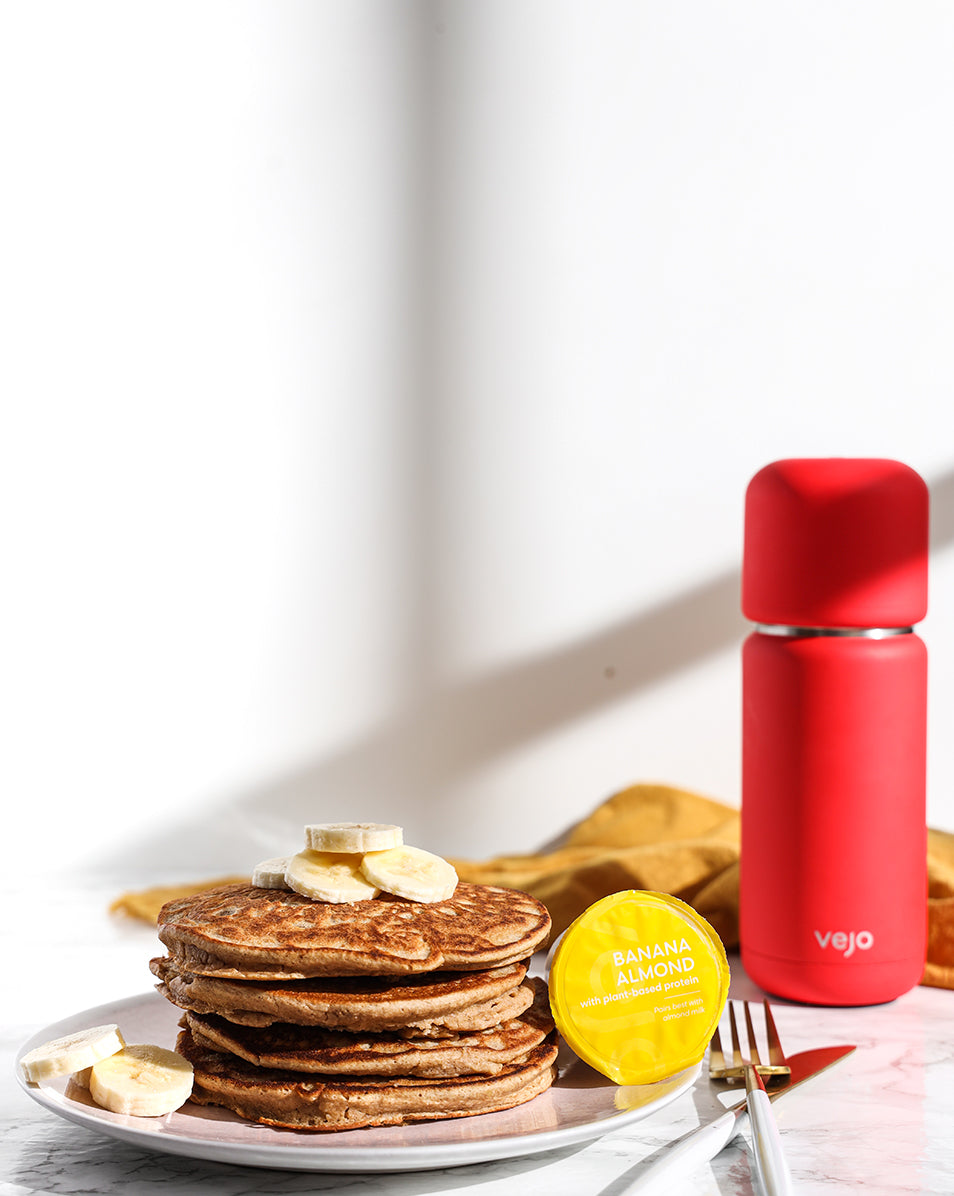 A stack of savory banana pancakes beside a yellow banana almond Vejo blend and red Vejo blender.
