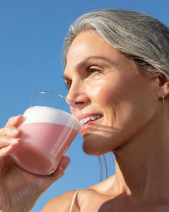 A woman standing outside against a deep blue sky drinking a Vejo Collagen Glow smoothie.