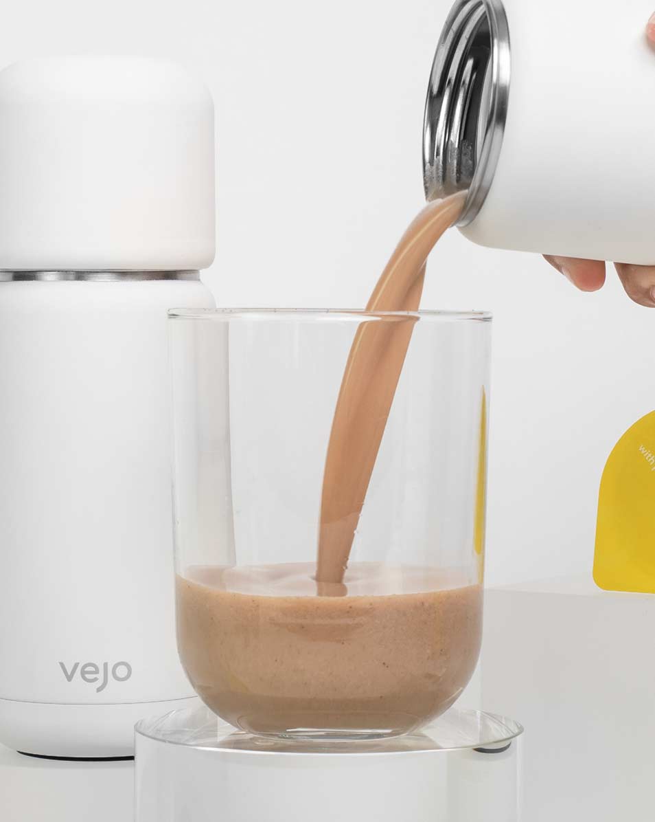 Vejo’s Banana Almond blend being poured into a clear glass by a white Vejo blender.