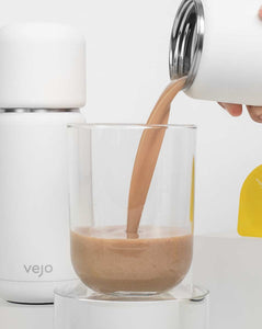 Vejo’s Banana Almond blend being poured into a clear glass by a white Vejo blender.